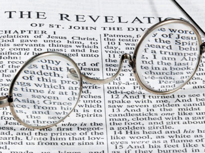 The book of Revelation in the Bible with old-fashioned glasses laying on top