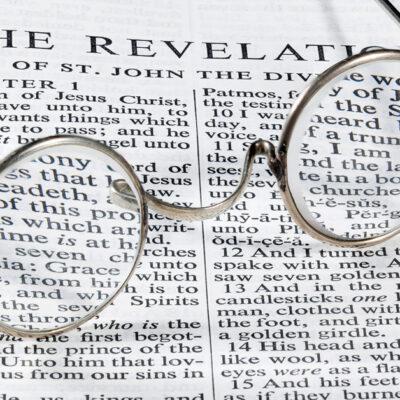The book of Revelation in the Bible with old-fashioned glasses laying on top