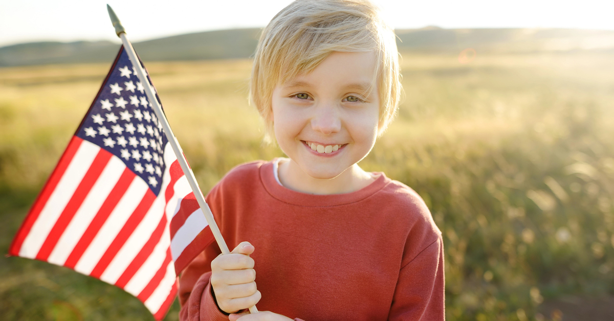 Cute blonde boy holding American flag in field