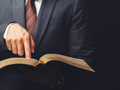 Man in suit and tie pointing to an open Bible