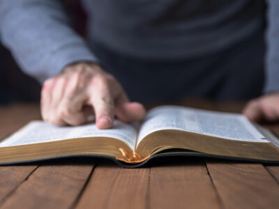 Man pointing out something in a Bible on a wooden table