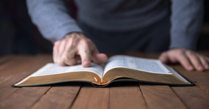 Man pointing out something in a Bible on a wooden table
