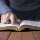 Man pointing out something in a Bible on a wooden table